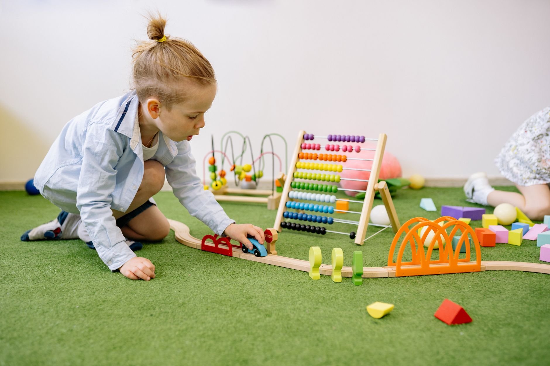 Young child playing with colorful educational toys indoors on a green carpet.